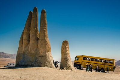 白天，人们坐在黄色公共汽车附近的棕色沙滩上